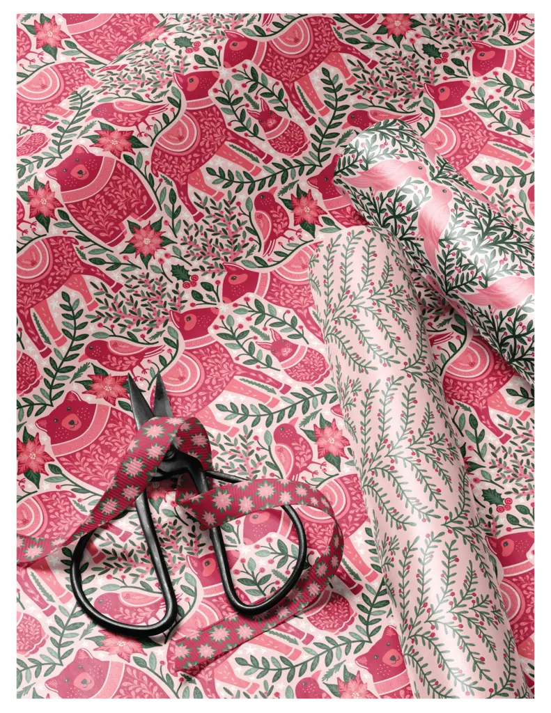 A flat lay image featuring festive pink and red patterned fabric with folk animal designs, along with a pair of black scissors and decorative ribbon on top.