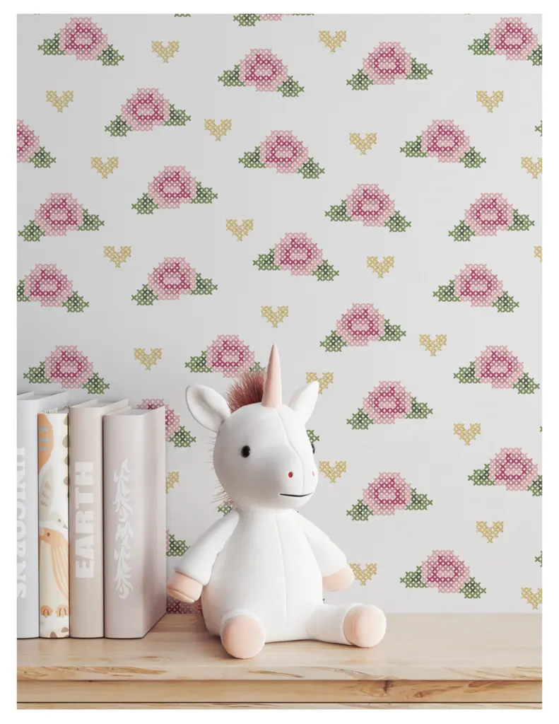 A children's room decor scene featuring a soft unicorn toy sitting on a wooden shelf next to pastel-colored books, with a floral cross-stitch pattern wallpaper behind.