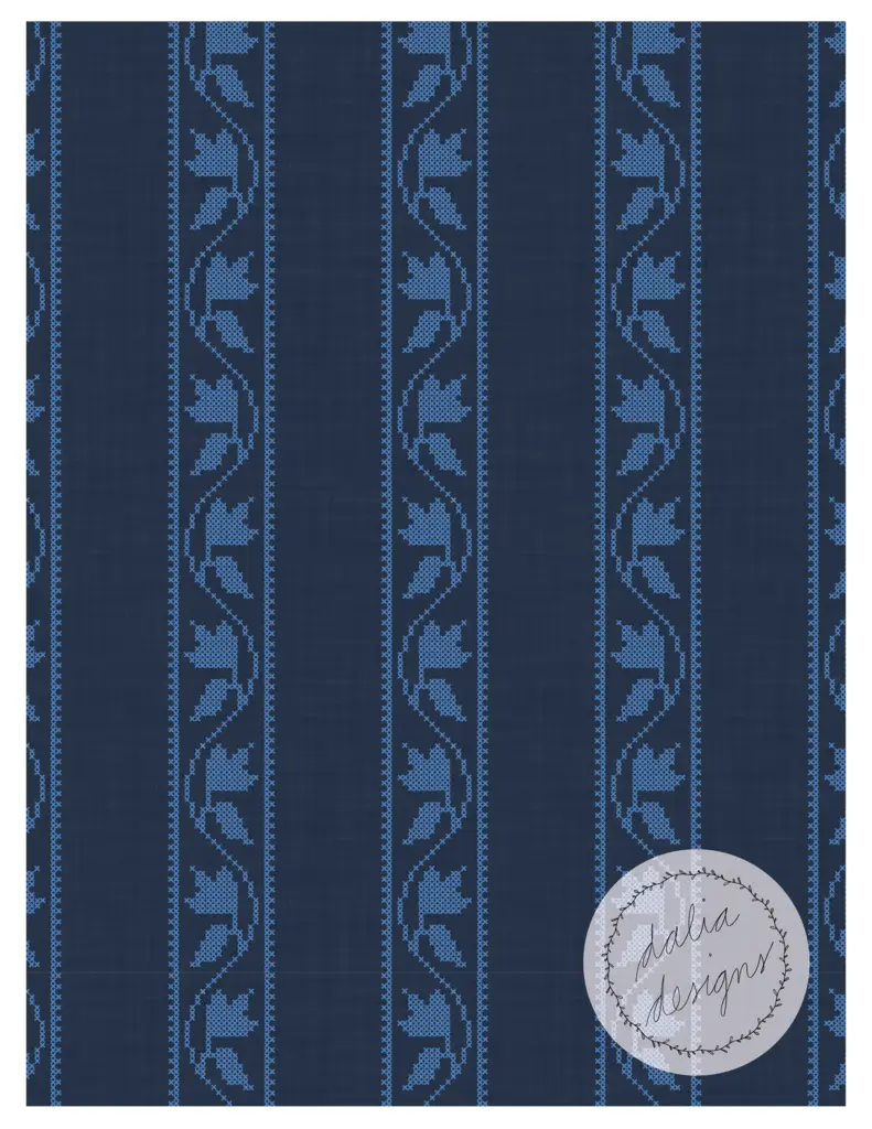 A denim blue patterned fabric featuring stylized floral motifs in a cross-stitch design, with intricate vine patterns and a subtle checkered texture.