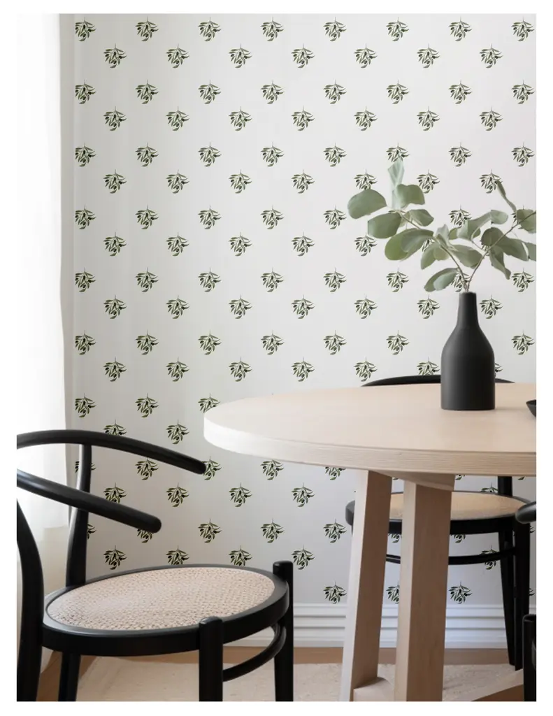 A cozy dining area featuring a round wooden table, black chairs, and a decorative plant in a black vase against a leaf-patterned wallpaper.