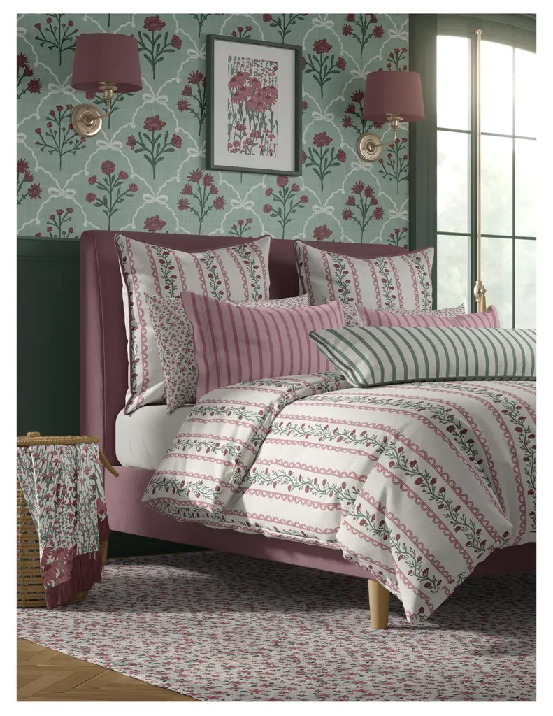 A beautifully arranged bedroom featuring a pink bed frame with floral patterned bedding and cushions, set against a floral wallpaper. The room includes matching bedside lamps and a floral area rug.
