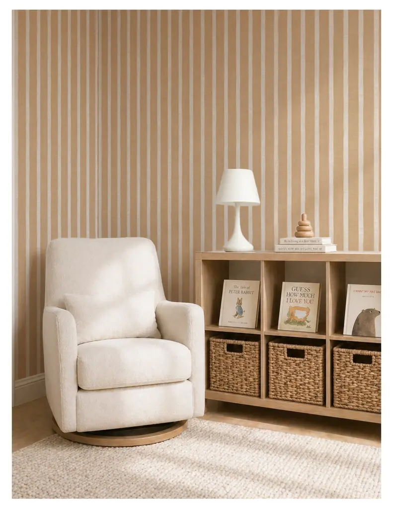 A cozy living space featuring a cream-colored swivel chair, a white lamp on a shelf, and a wooden bookshelf with woven baskets and a collection of children's books against a striped beige wall.