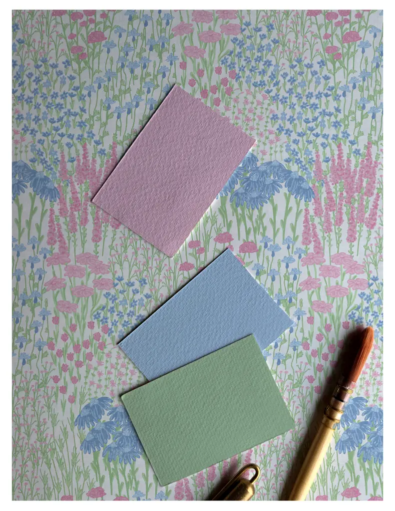 Three color swatches (pink, blue, and green) placed on a floral patterned background with a brush and pen.